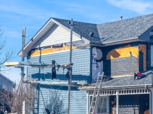 A residential house under renovation, with scaffolding, exposed framing, and new light blue siding partially installed. A ladder leans against, siding contractors East Peoria IL, siding company East Peoria IL, vinyl siding East Peoria IL, siding installation East Peoria IL, siding replacement East Peoria IL, siding contractors near East Peoria IL, house siding contractors East Peoria IL, exterior remodeling East Peoria IL, soffit and fascia East Peoria IL, vinyl siding contractors East Peoria IL, siding repair East Peoria IL, home siding replacement East Peoria IL, insulated siding East Peoria IL, residential siding contractor East Peoria IL, low maintenance siding East Peoria IL, siding installers East Peoria IL, curb appeal siding East Peoria IL, siding estimate East Peoria IL, Norandex siding East Peoria IL, Mastic siding East Peoria IL, siding services East Peoria IL